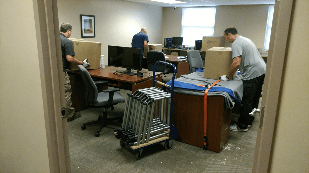 Movers relocating office furniture and boxed equipment