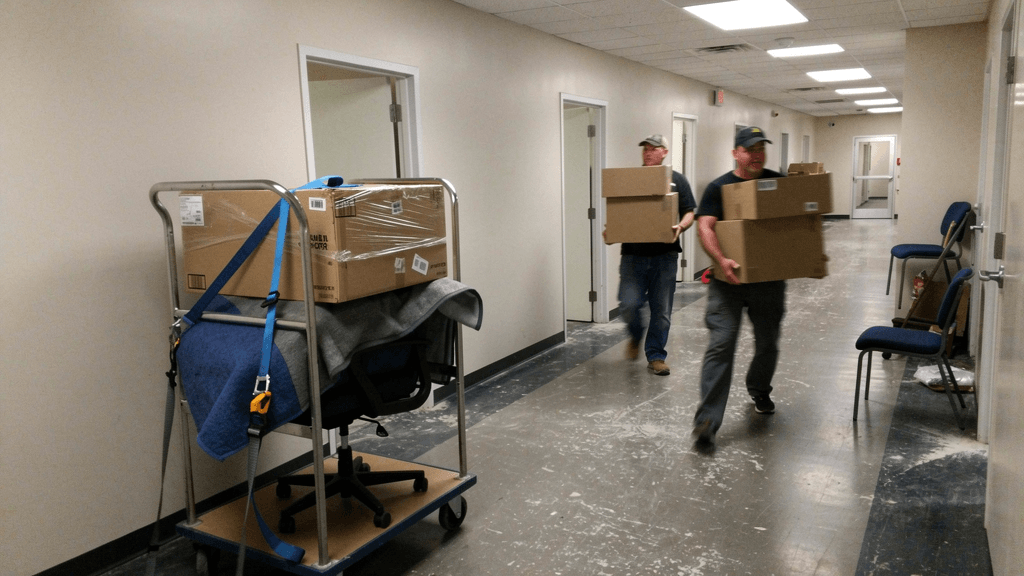 Movers carrying office chairs and boxed files during a workplace move