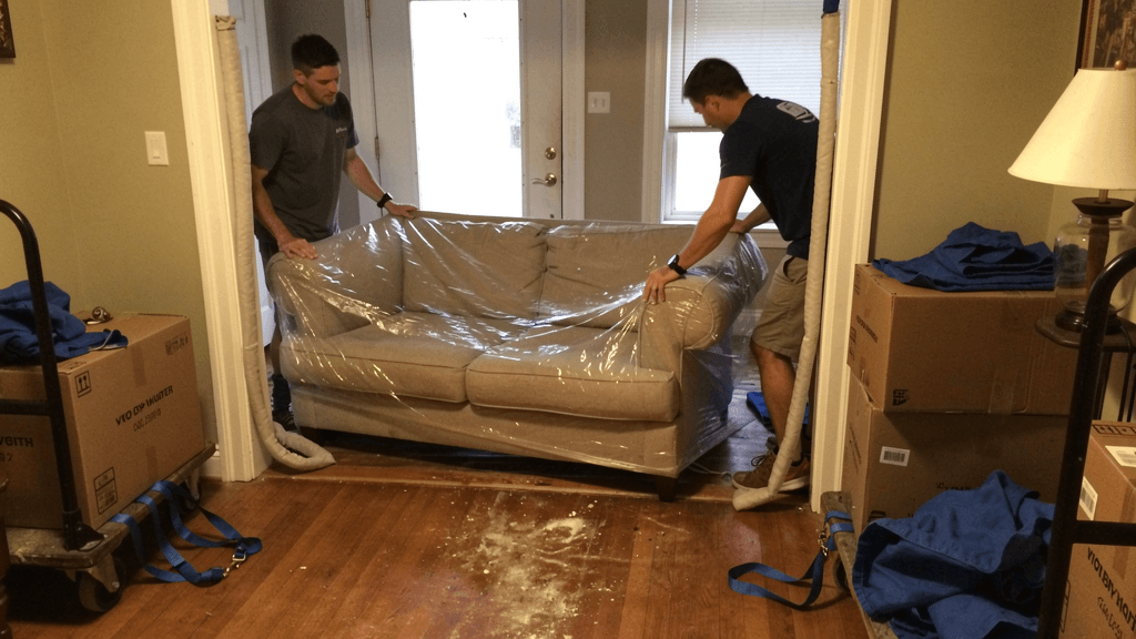 Movers carrying a wrapped sofa through a residential doorway